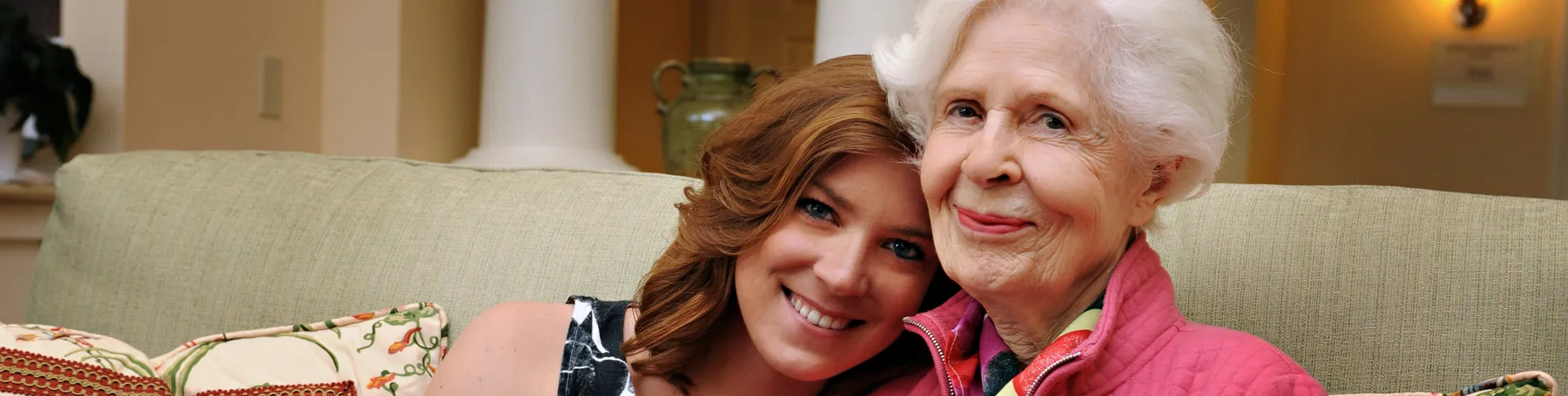 A resident and staff member smiling together on a couch