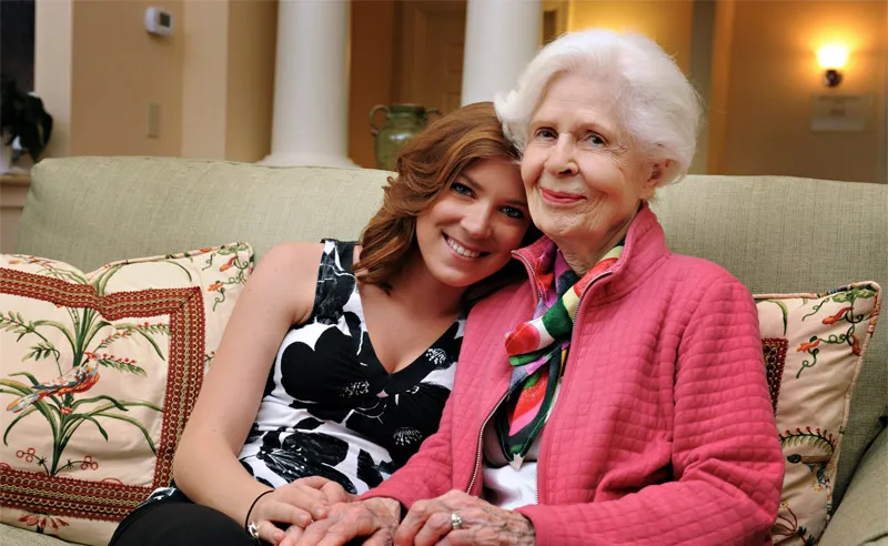 A woman with a senior resident smiling together on a couch