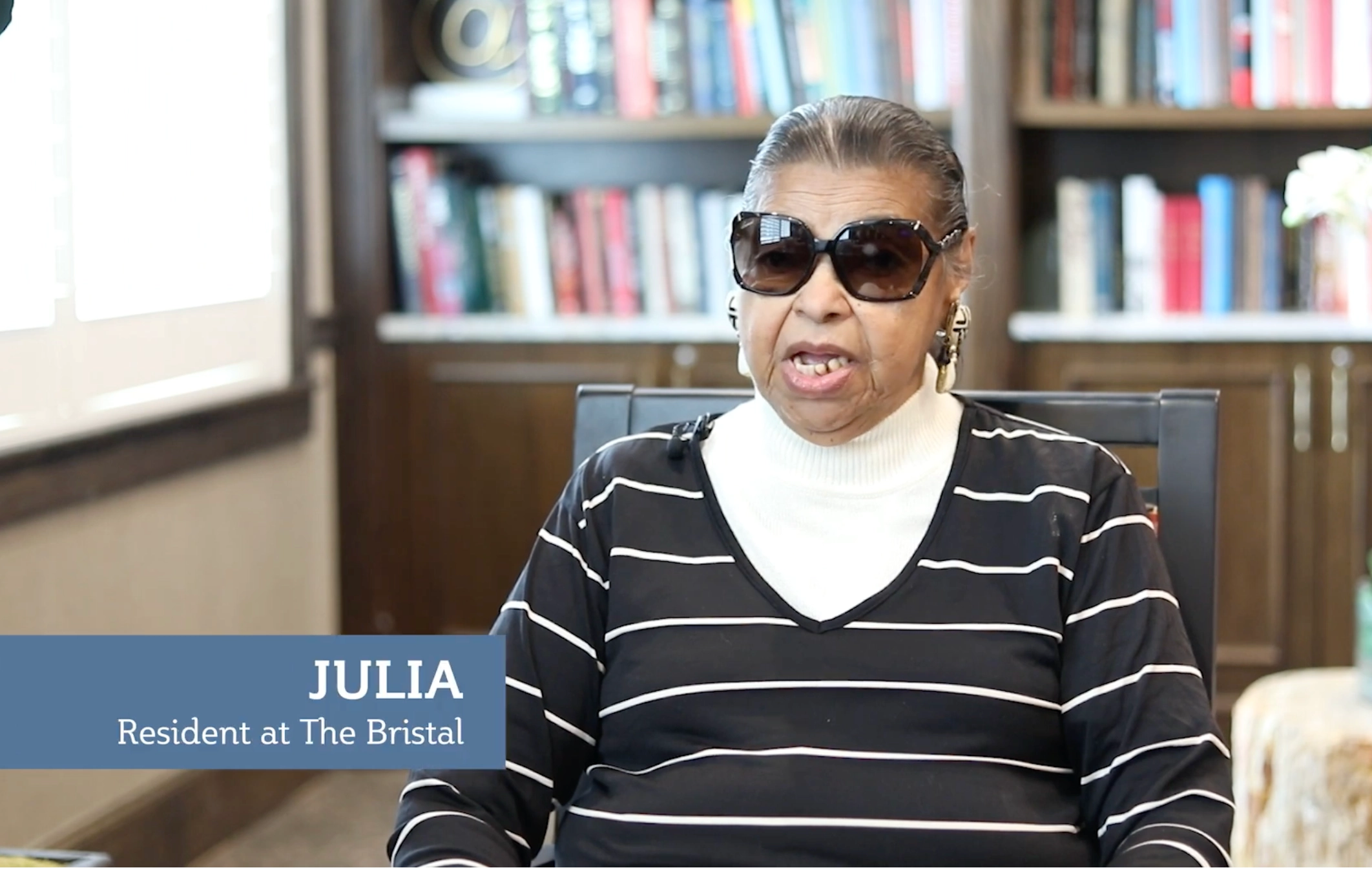 Resident Julia seated in a common area with bookshelves behind her