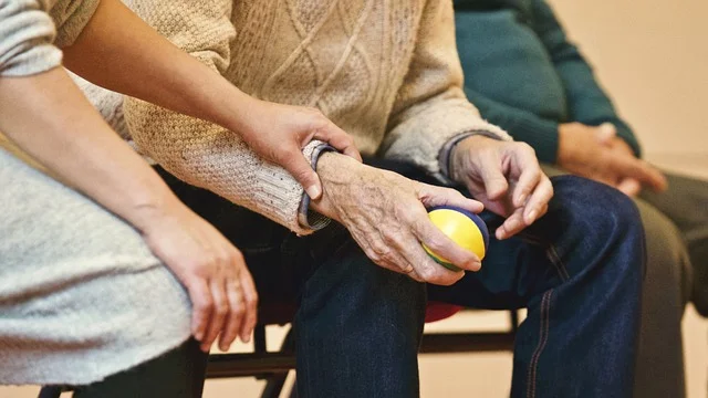 Hands of a caregiver and senior holding a ball.