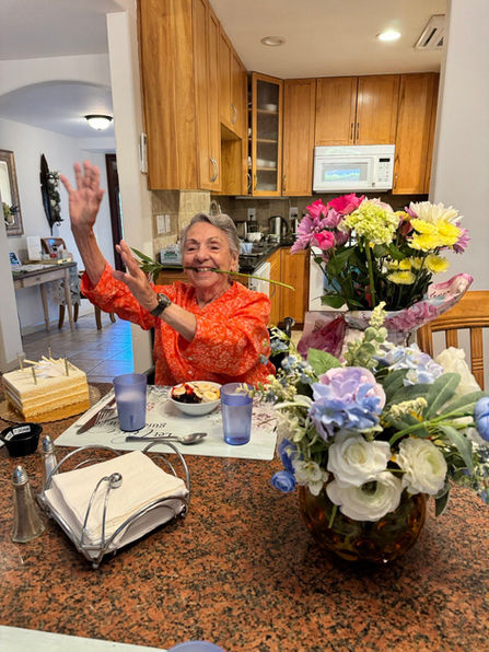 A resident smiling and waving at a dining table.