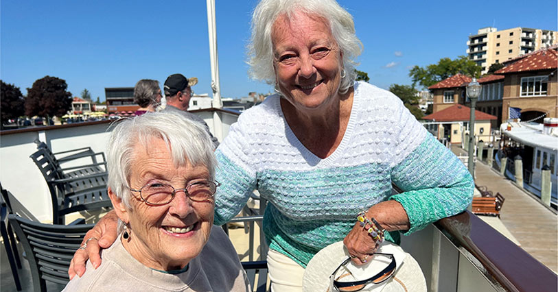 Two smiling women enjoying a sunny outdoor scene.