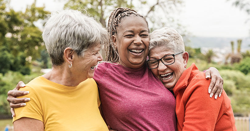 Three elderly women joyfully embracing outdoors.