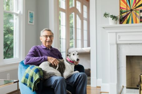Senior man smiling with a dog in a bright interior.