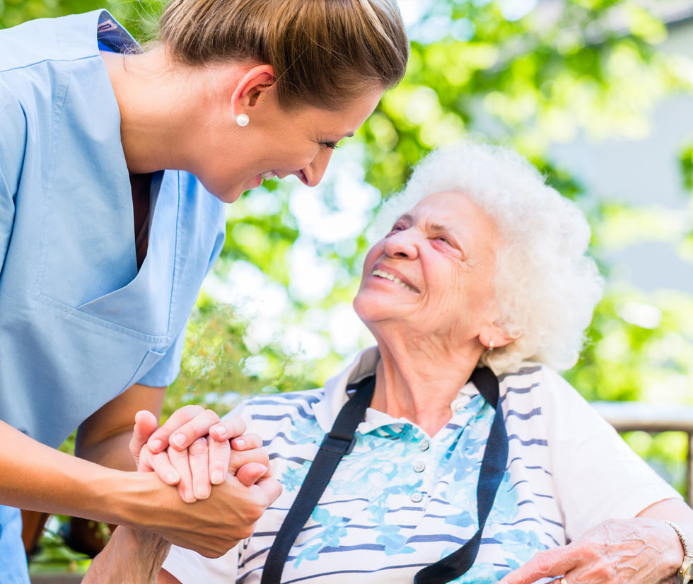 Caregiver interacting with a smiling elderly woman outdoors.