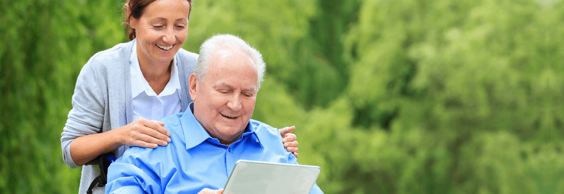 Caregiver assisting an elderly man with a tablet outdoors