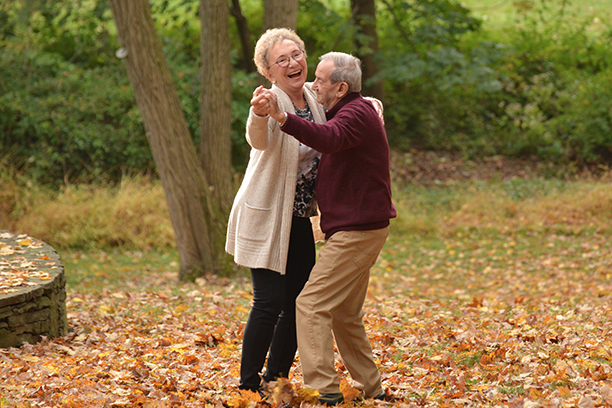 Senior couple dancing joyfully in autumn leaves.