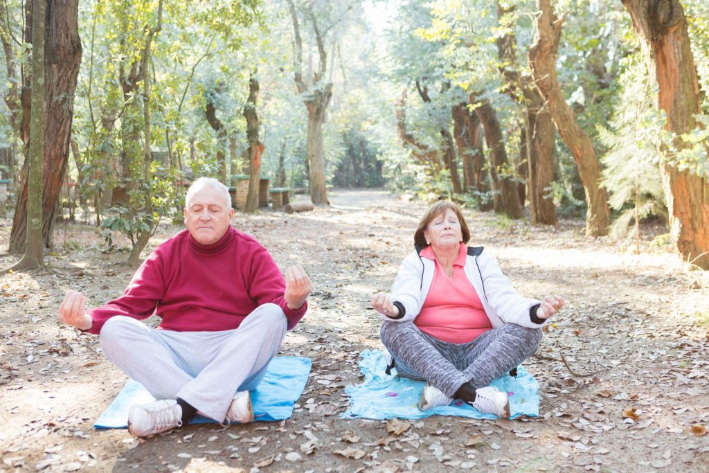Seniors meditating outdoors in a wooded area.