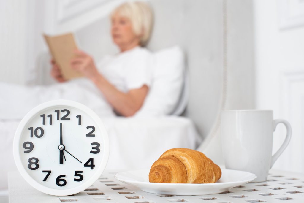 A senior woman reading in bed with breakfast items.