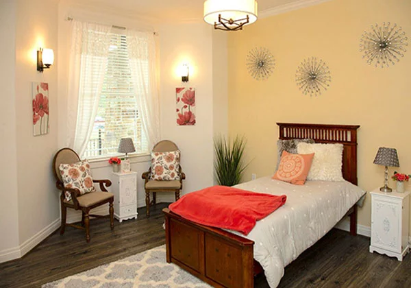 Well-decorated private resident room with bed and chairs.