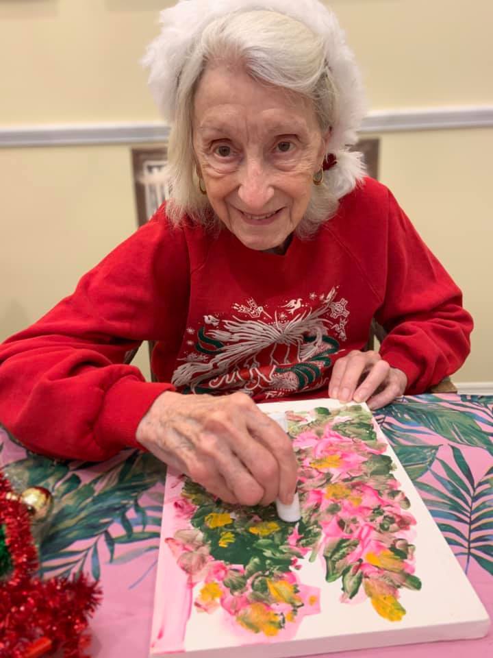 Elderly woman painting flowers in a festive setting.