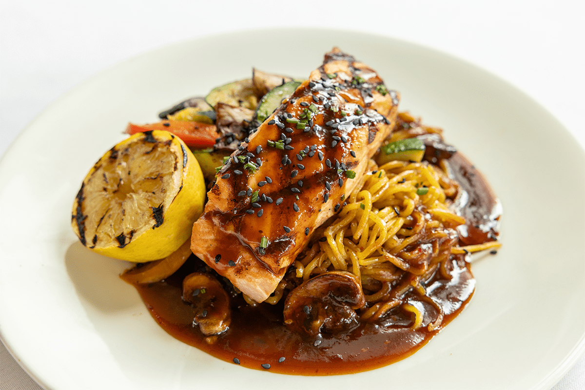 A plate of grilled salmon with vegetables and noodles