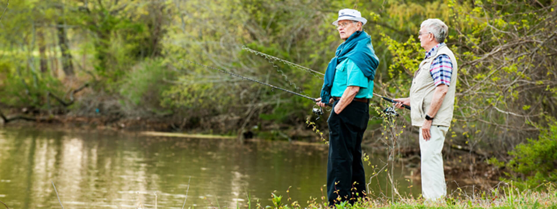 Two elderly men fishing by a calm pond