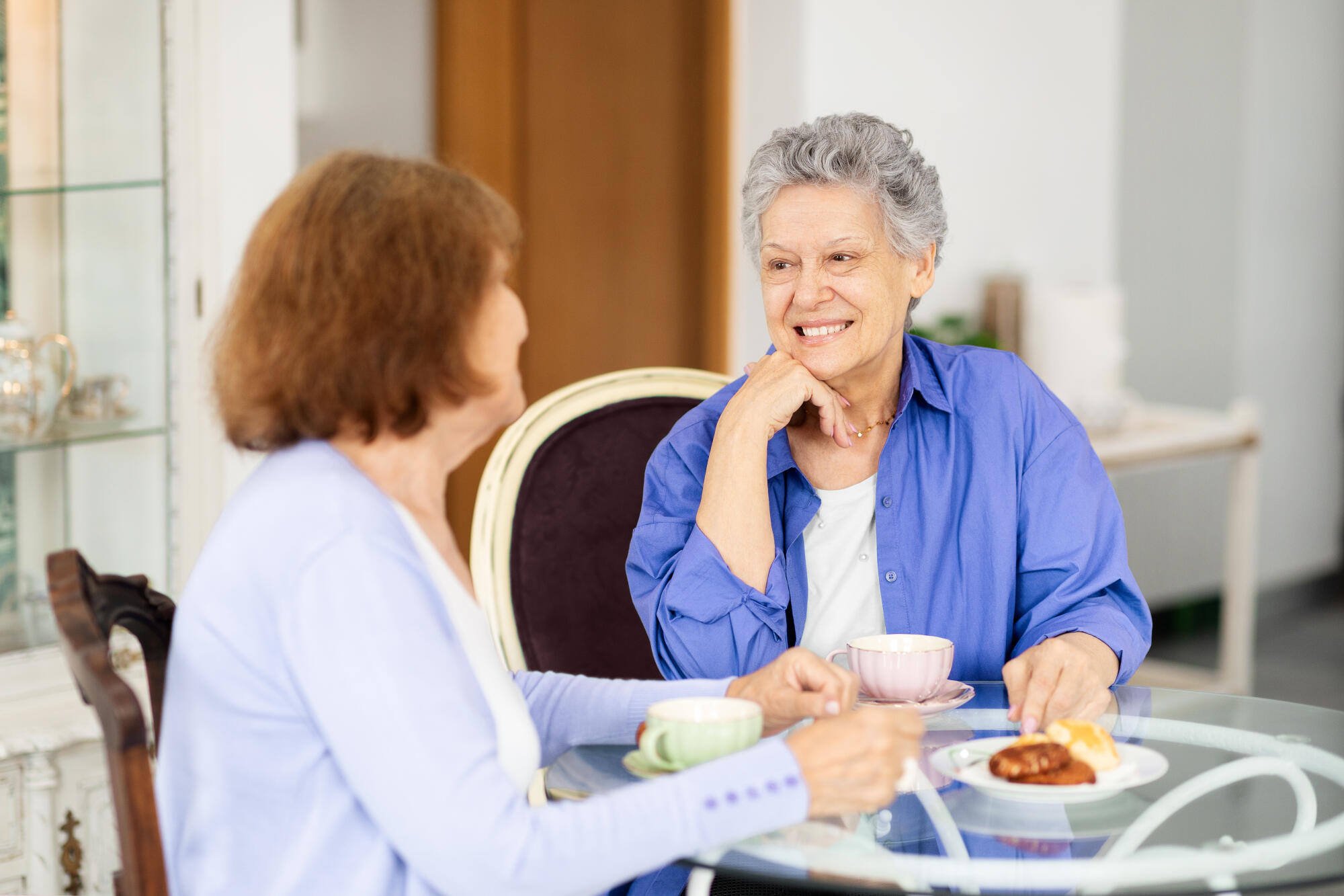 Two seniors enjoying tea and pastries in a bright common area