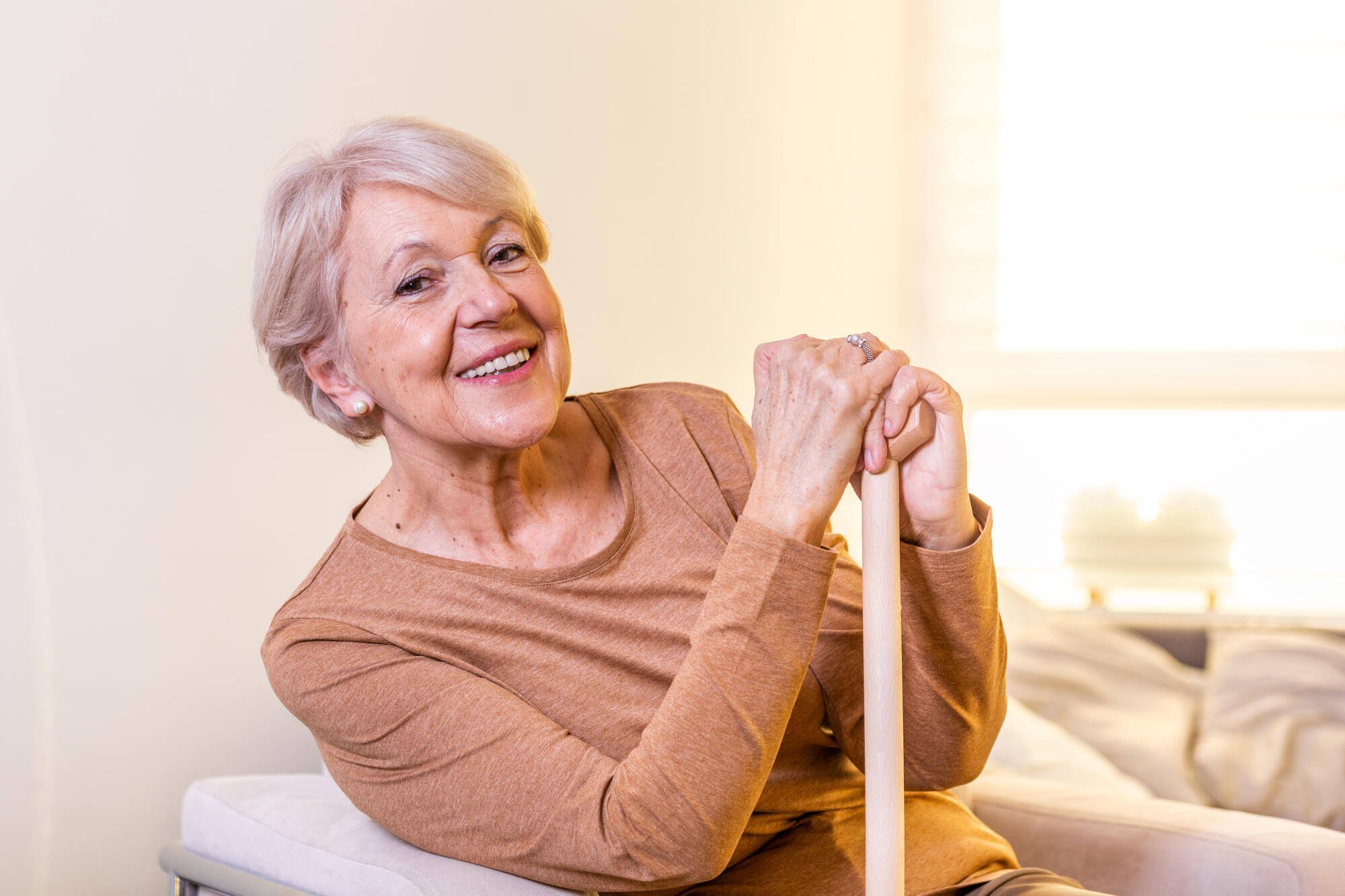 A smiling elderly woman seated indoors with a cane