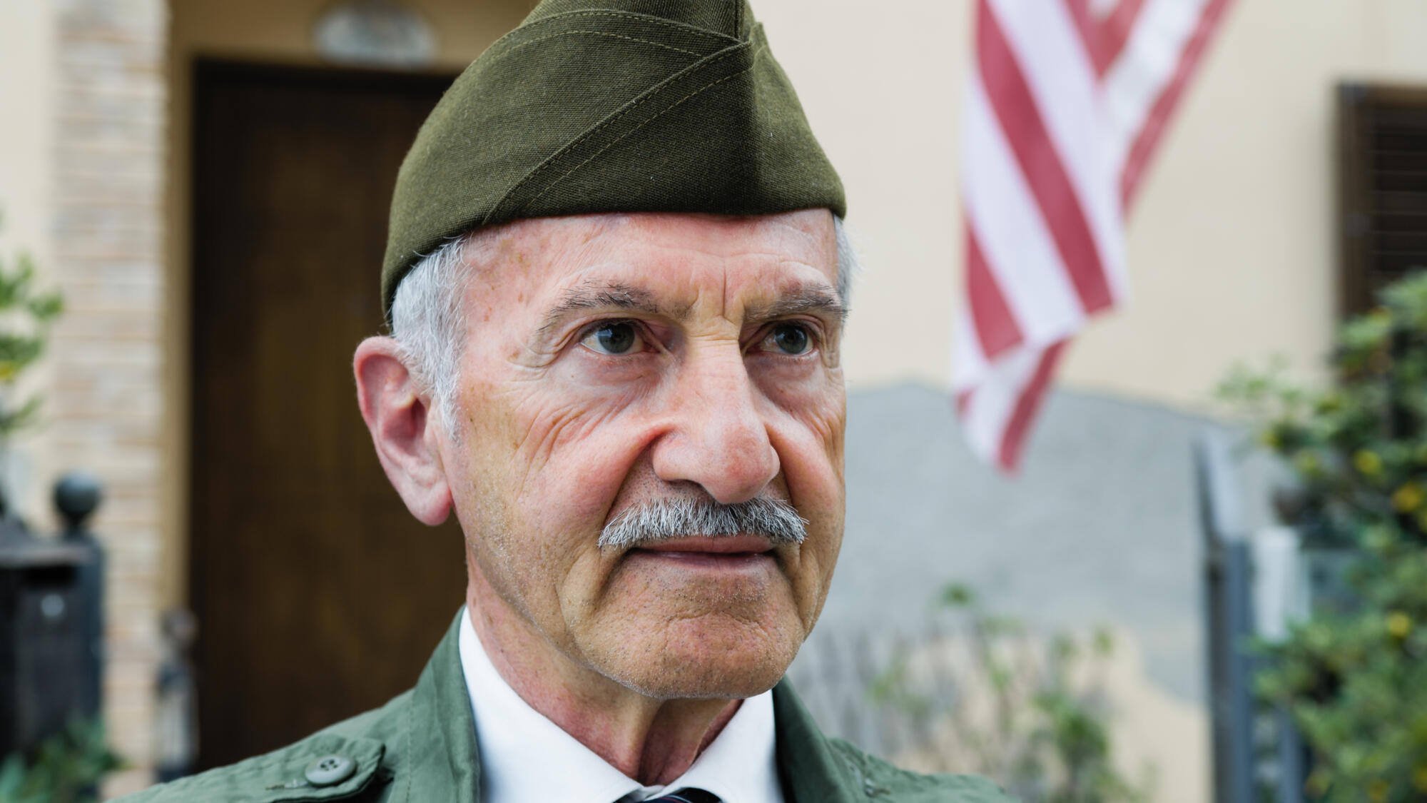 An elderly man in military attire with an American flag in the background