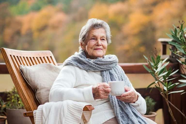An elderly woman enjoying tea on a balcony