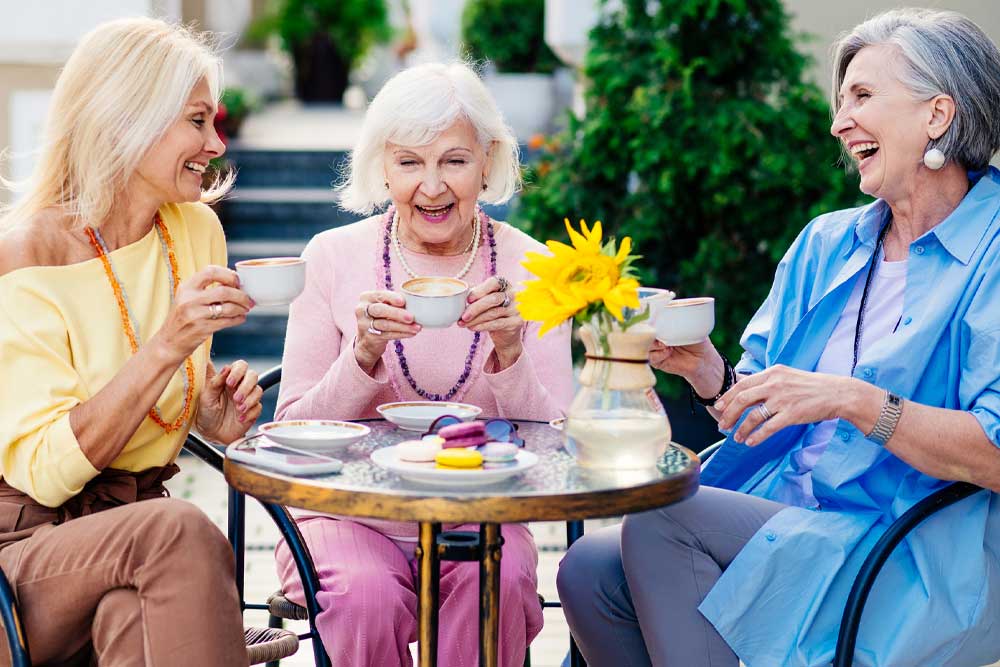 Three smiling women enjoying tea in a garden