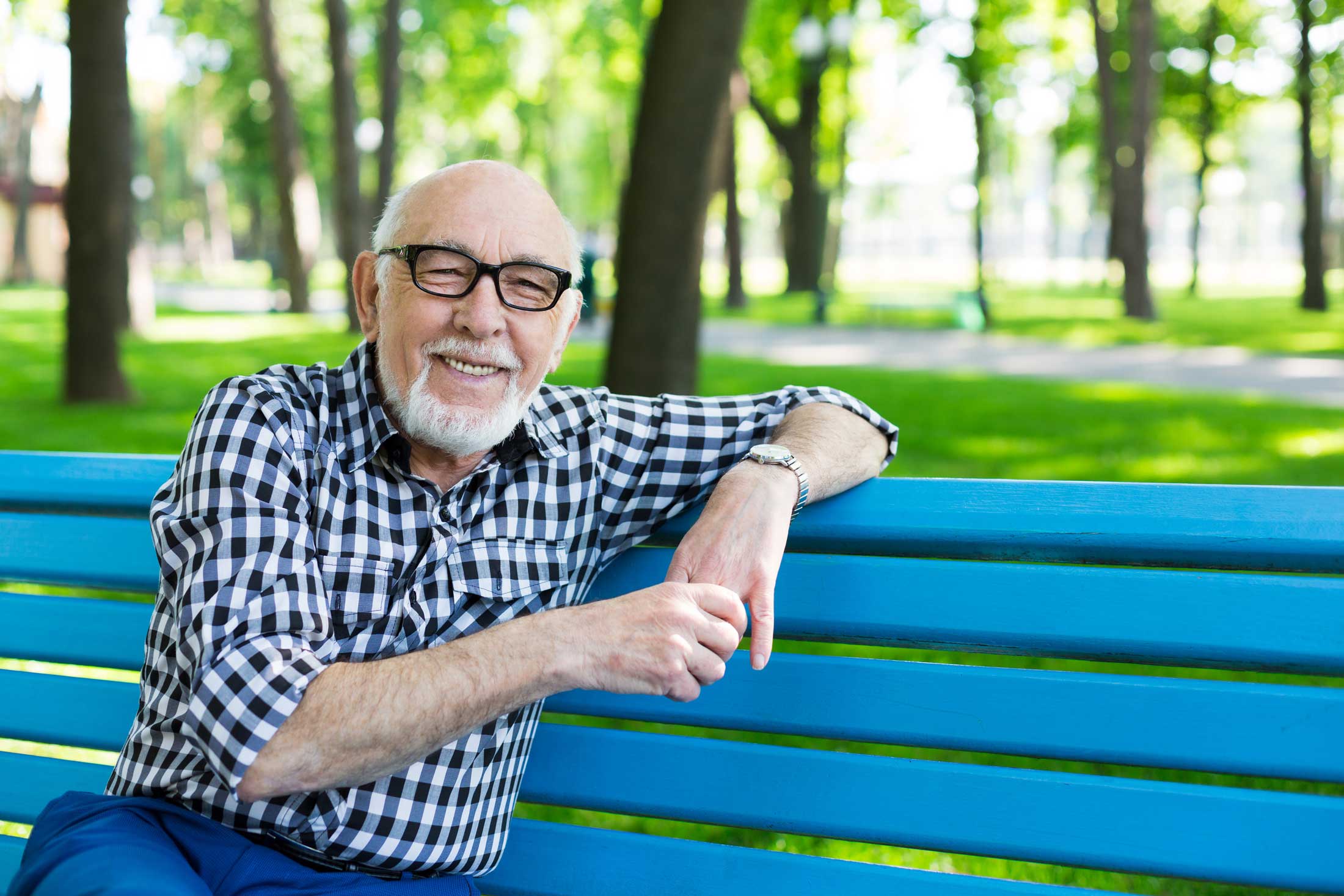Smiling senior man sitting on a blue park bench