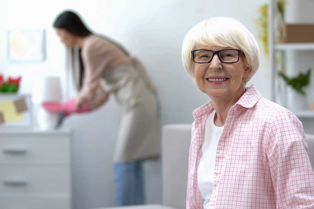 Smiling resident with caregiver in the background