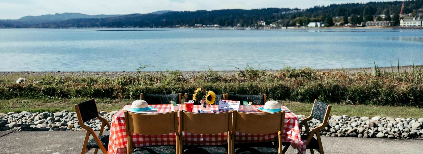 Outdoor dining setup by the water with checkered tablecloth.