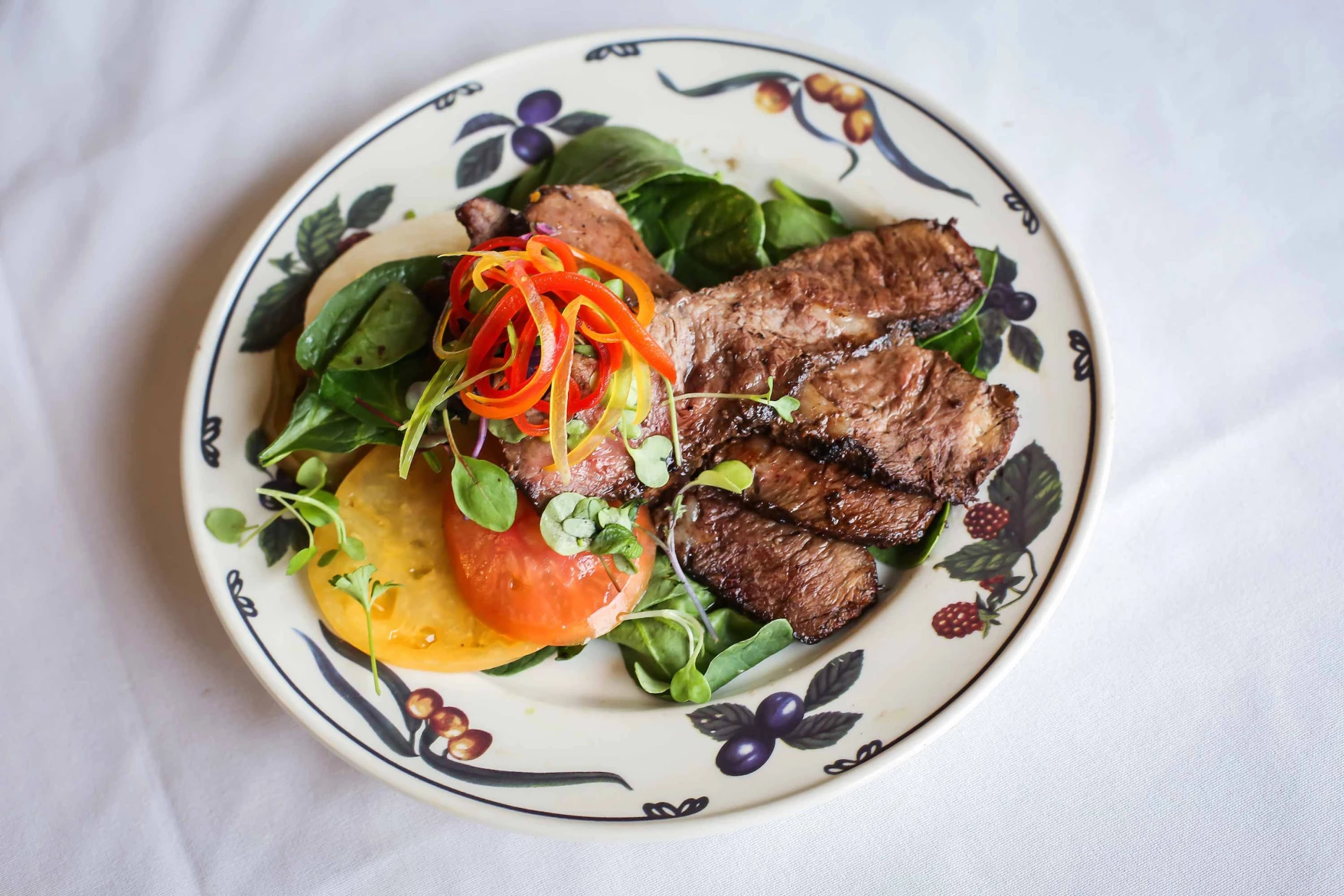 A plate of grilled steak with salad and tomato