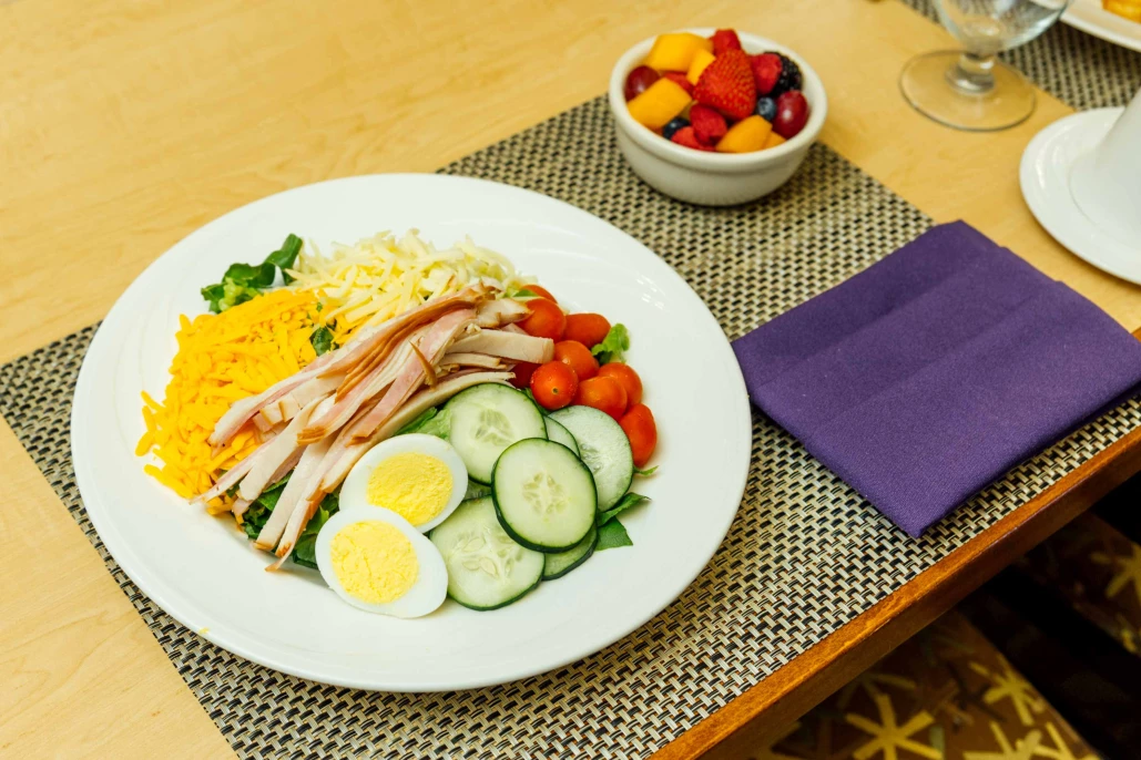 A plated salad with various ingredients and a side of fruit