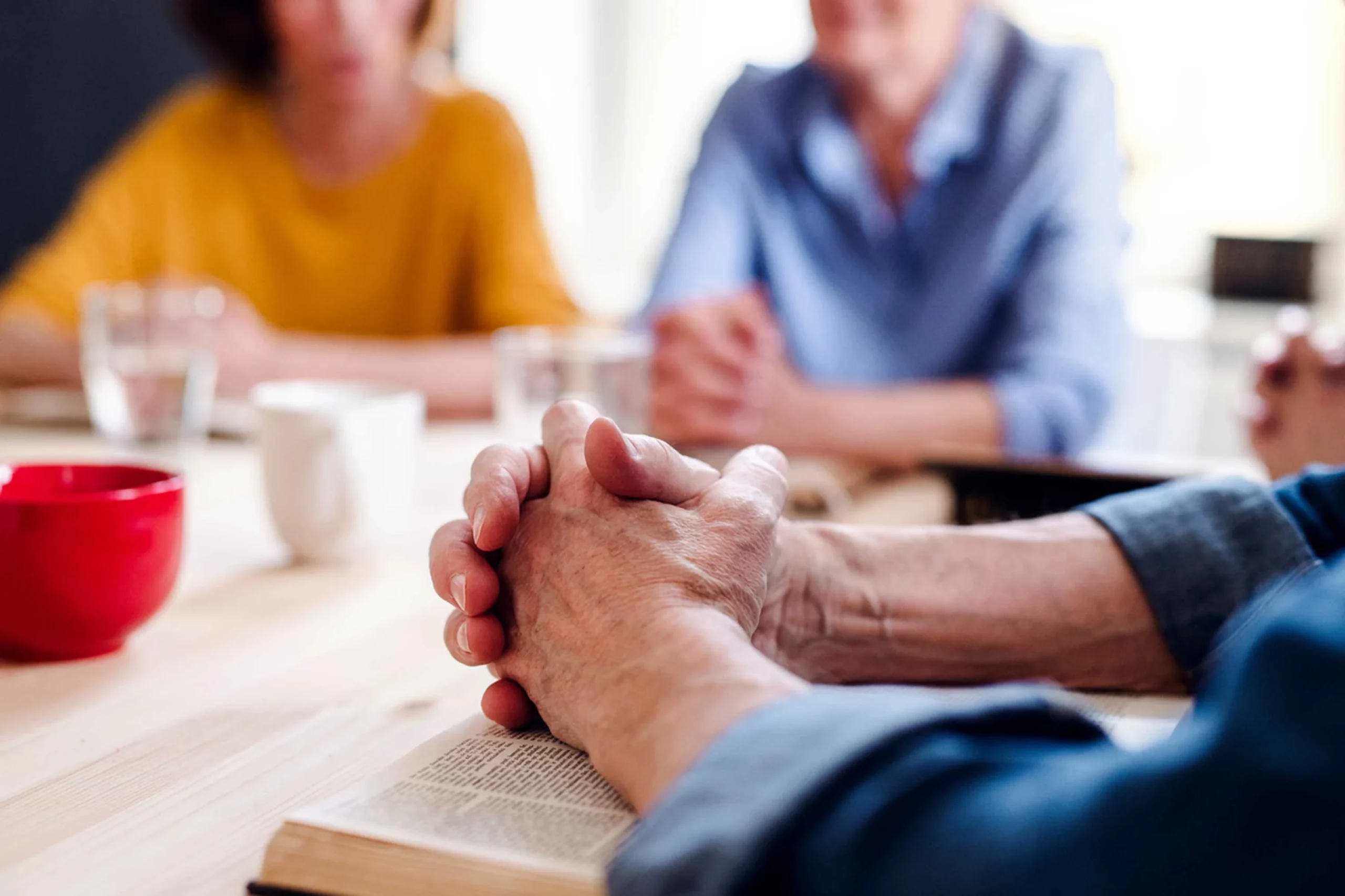 Close-up of elderly hands clasped during a group discussion