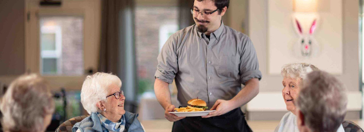 Staff serving food to smiling residents in dining area
