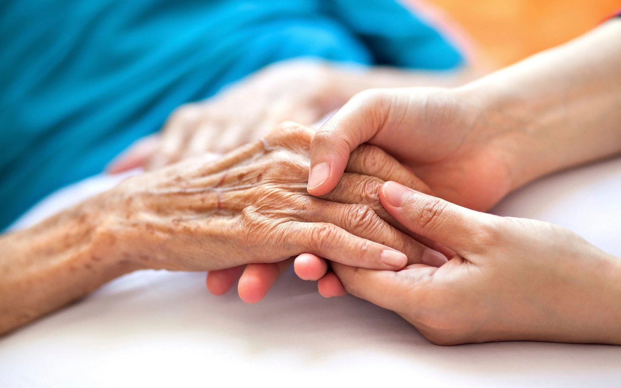 Hands of a caregiver gently holding an elderly person's hand.