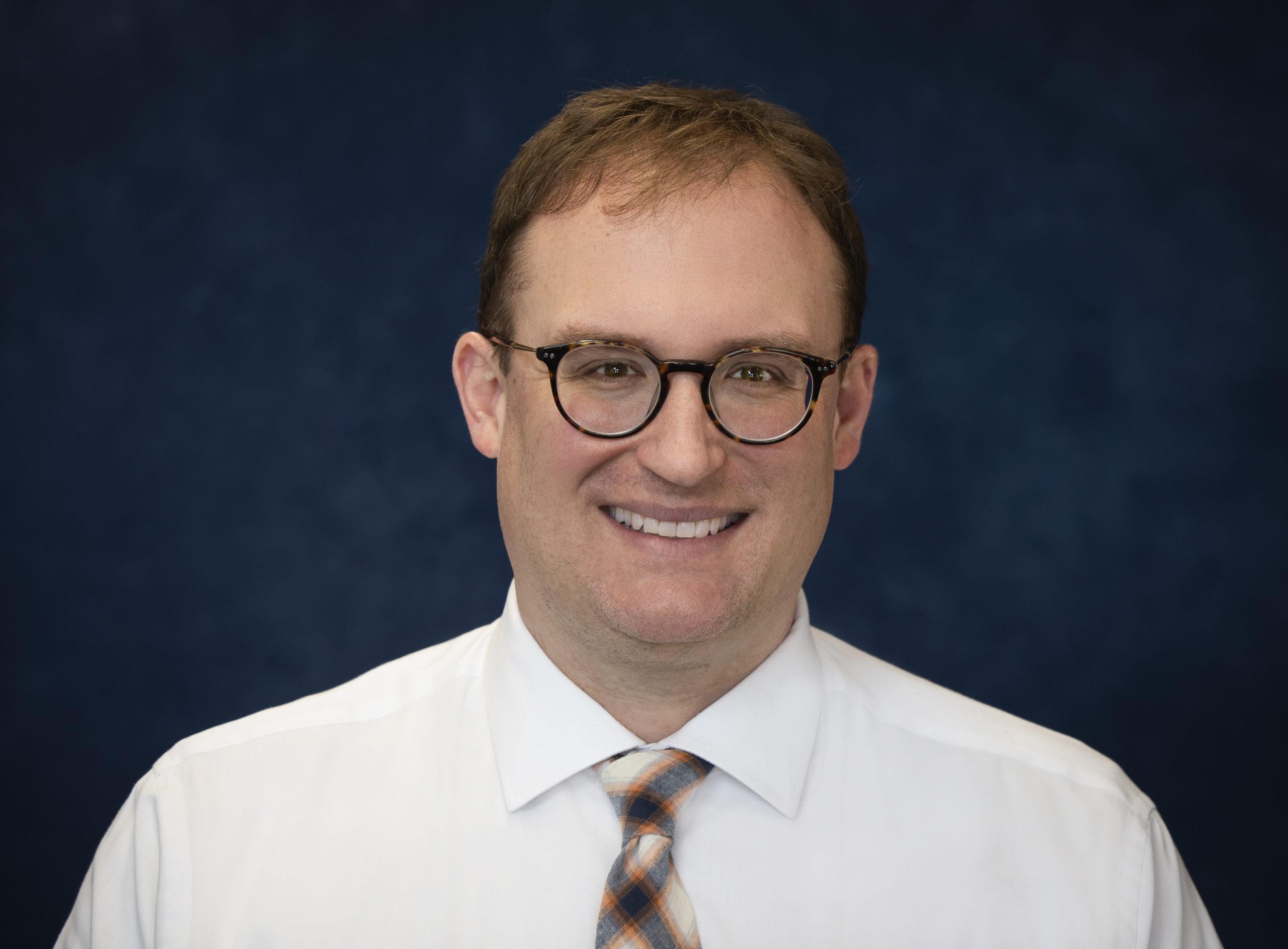 Male staff member smiling against a dark background