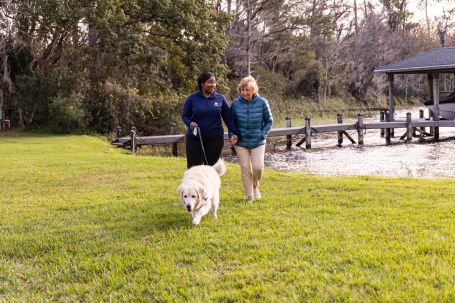 Resident and staff member walking a dog by the water.