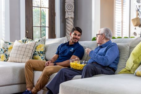 Caregiver chatting with elderly resident in a cozy living room.