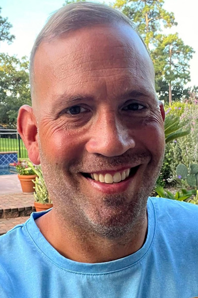 Smiling man outdoors with plants in the background.