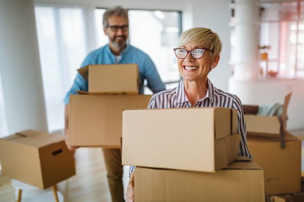 Happy seniors moving boxes indoors.