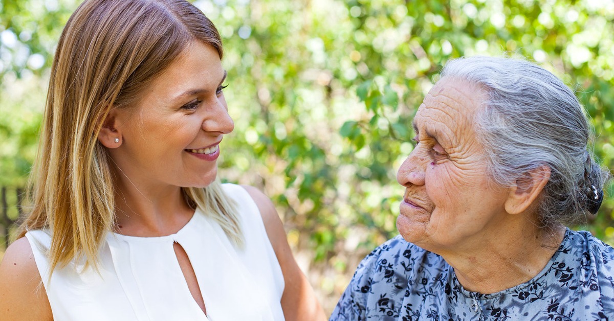 Caregiver interacting with an elderly woman outdoors.