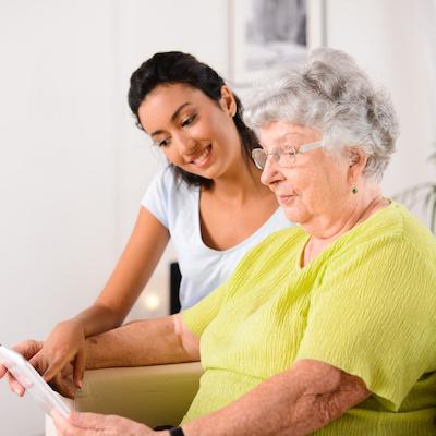 Caregiver assisting an elderly woman with a tablet.
