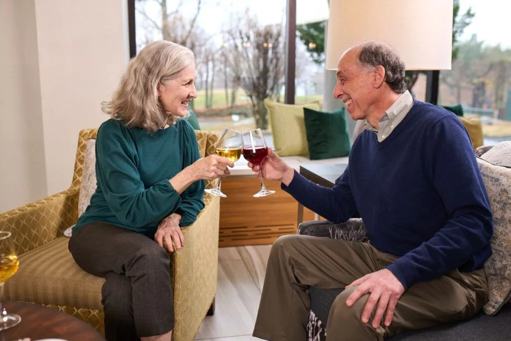Two residents toasting with drinks in a cozy setting.