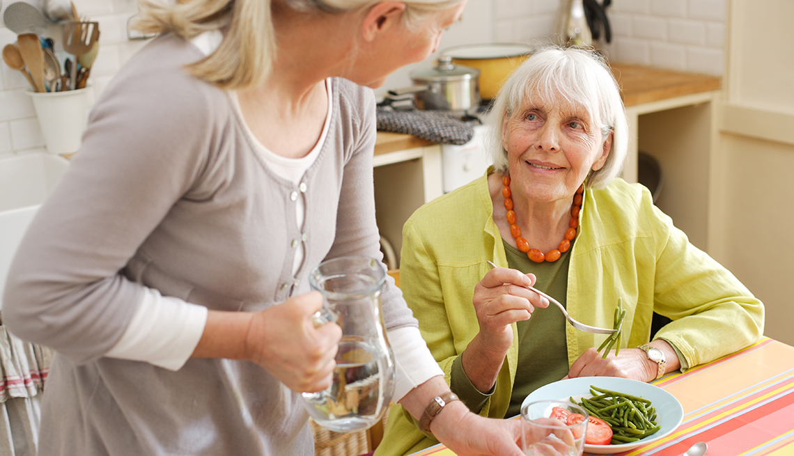 Caregiver serving food to a smiling senior woman.
