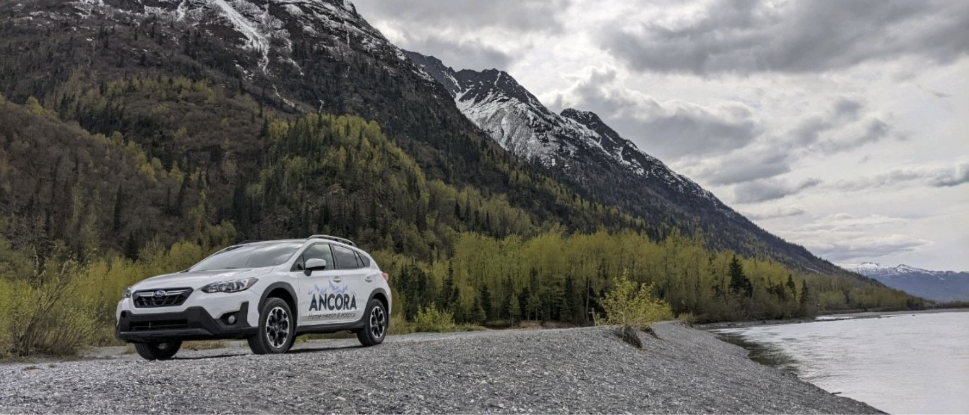 Vehicle parked by a river with mountains in the background.