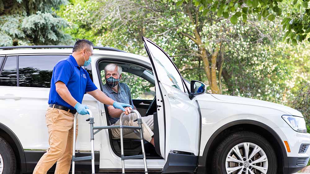 Caregiver assisting senior into a vehicle outdoors.