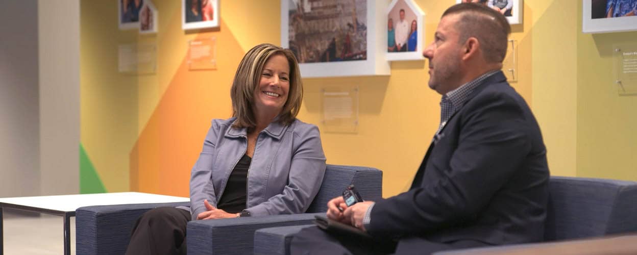 Two smiling individuals engaged in conversation indoors.