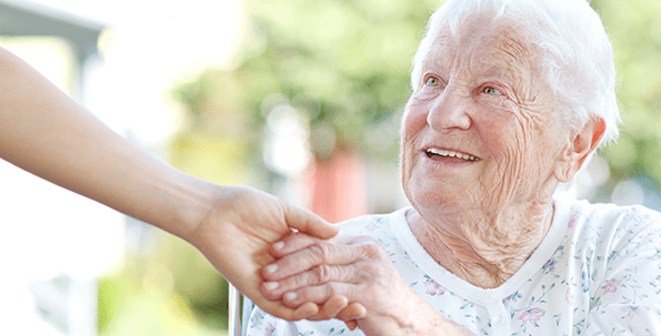 A caregiver holding hands with a smiling elderly woman.