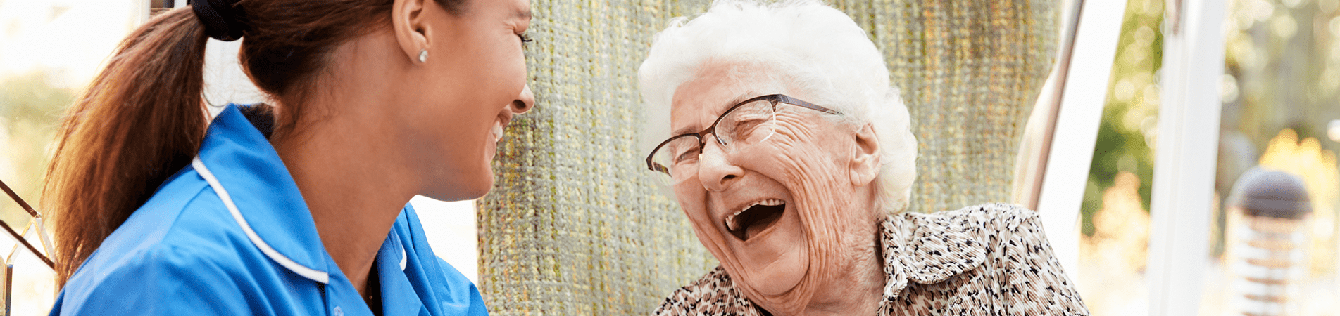 Caregiver and elderly woman laughing together outdoors.