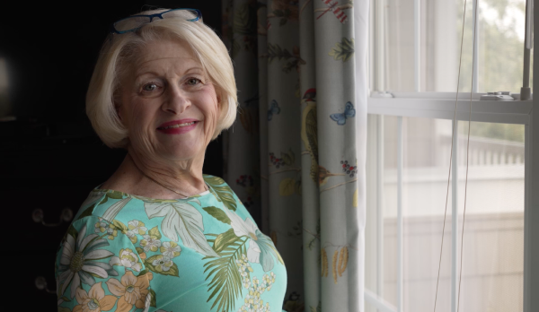Smiling woman by a window with floral curtains.