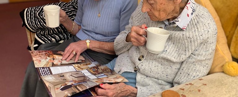 Two elderly women reading a magazine together.