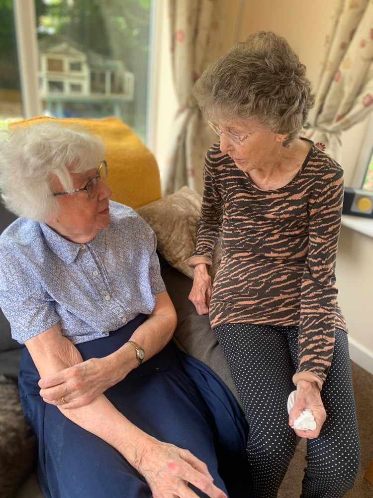 Two seniors engaged in conversation indoors.