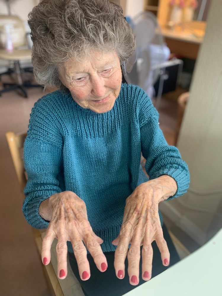 Elderly woman showing hands with red nails.
