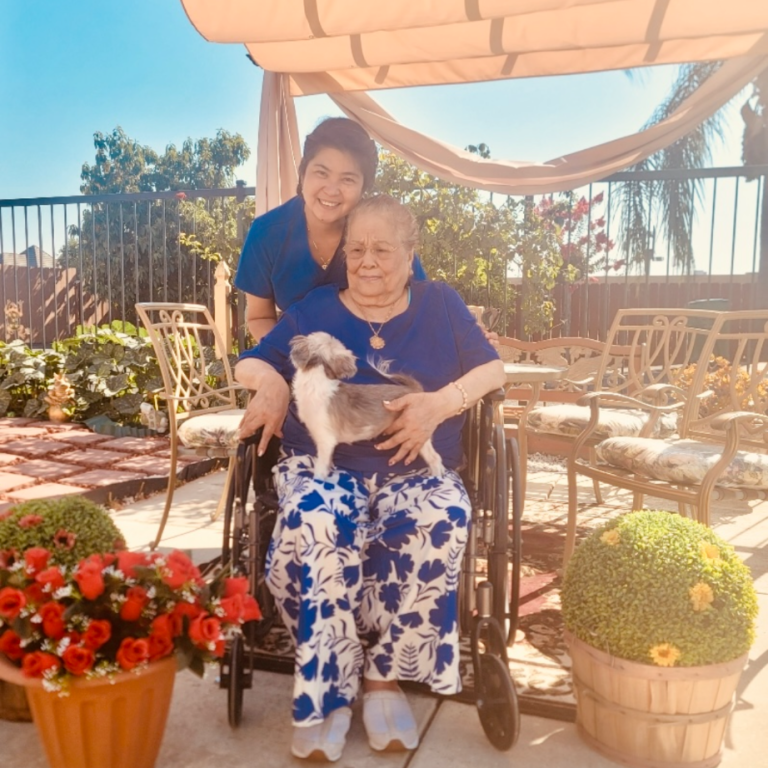 A caregiver with a resident holding a small dog outdoors.