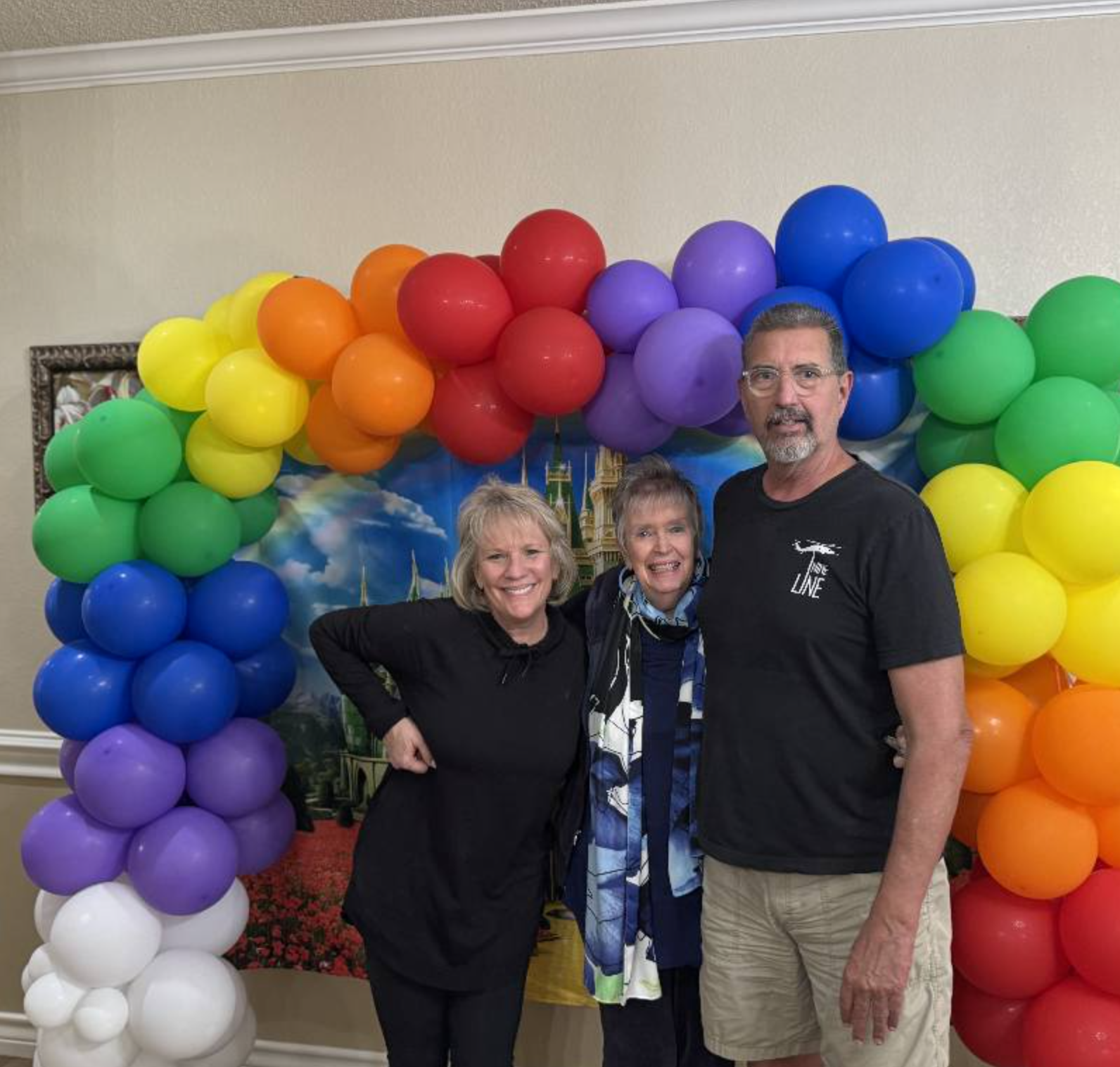 Three people smiling by a colorful balloon arch
